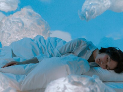 A sleeping woman surrounded by small weightless clouds, reflecting how sleep cycles help the body and mind reset