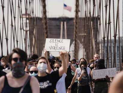 Protestor with a sign that reads "silence is violence" on the Brooklyn Bridge in New York, USA