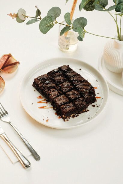 Un plato blanco con un trozo de brownie cubierto con chocolate derretido