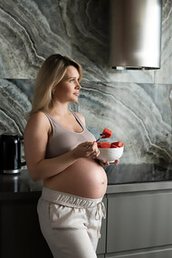 A medium shot of a pregnant woman enjoying a fruit bowl, emphasizing the benefits of nutritious food choices during pregnancy for both mother and baby