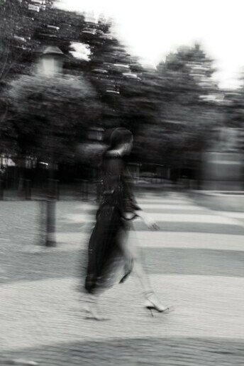 A black and white, blurred image of a woman walking down a city sidewalk