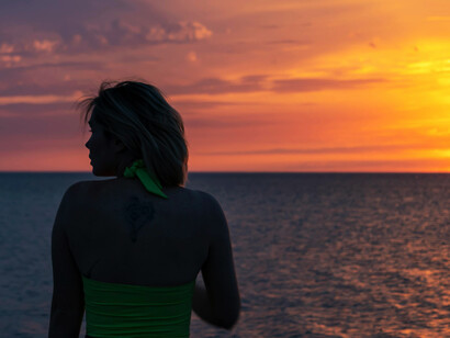 Back view of a woman standing by the sea at sunset