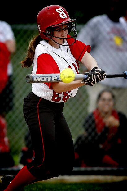 A female player grips her bat, ready to swing in a women’s baseball game