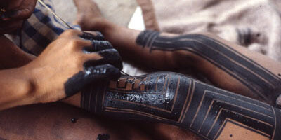 A Kayapó woman painting her daughter’s legs with genipa americana and charcoal. Photo: Darrell Posey, circa 1986. © Pitt Rivers Museum, University of Oxford (2001.82.1362).