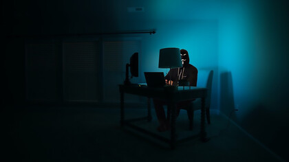 A man at a computer disguised as an anonymous hacker wearing a Guy Fawkes mask.
