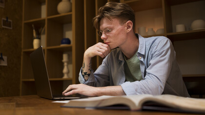 A young man studies in a virtual classroom and in a library, focusing on academic writing