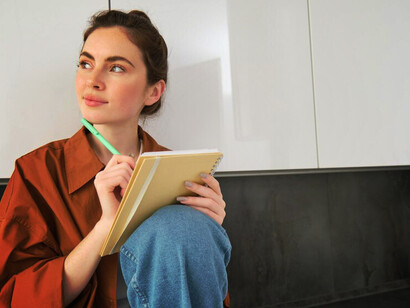 The essence of modern contemplation with a portrait of a young woman seated in her kitchen, gazing into the distance, lost in daydreams, while holding a notebook and pen