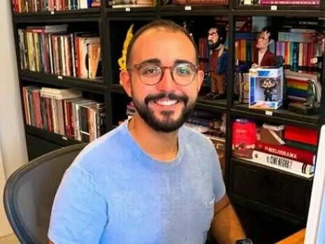 Raphael Montes posa diante de uma estante repleta de livros, em um ambiente que evidencia sua relação com a literatura. O escritor construiu sua trajetória explorando o suspense, o crime e os aspectos mais sombrios da psique humana