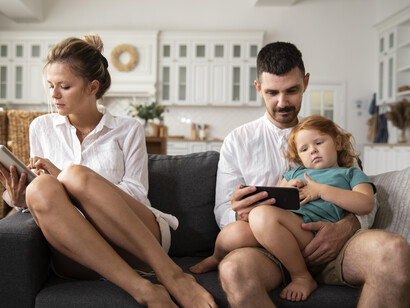 A family sits together in the living room, each absorbed in their devices, with little to no interaction