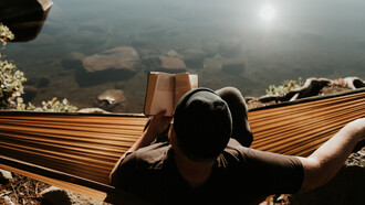 Hombre lee un libro recostado en una hamaca