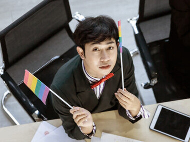 Confident and happy Asian gay businessmen collaborating in the office, dressed in formal attire. LGBTQ+ colleagues work together at the table, using laptops with pride and professionalism