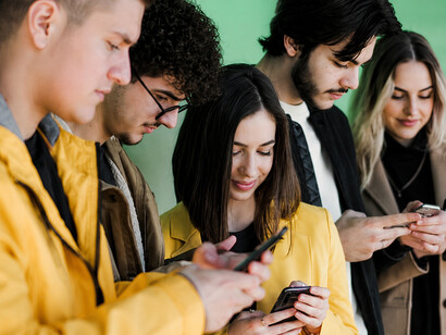 A group of young people stand together, each focused on their smartphone rather than interacting with one another