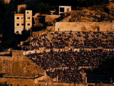 A bustling Roman theatre at sunset, filled with people and reflecting the vibrant atmosphere of local culture and community life