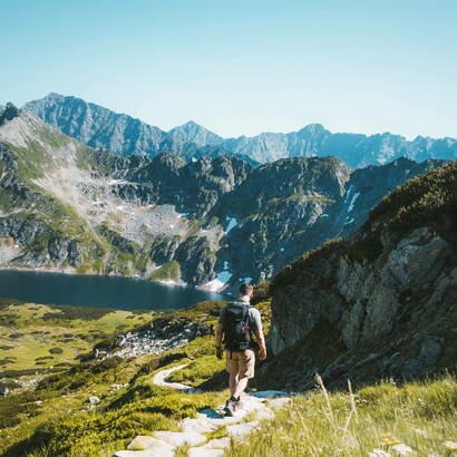 Uomo che cammina su un sentiero in pietra in un paesaggio montano: “Respirare aria fresca, lontano dall’inquinamento cittadino, è un toccasana per i polmoni, mentre l’esposizione al sole aiuta il corpo a produrre vitamina D, essenziale per la salute delle ossa e per il buon funzionamento del sistema immunitario”