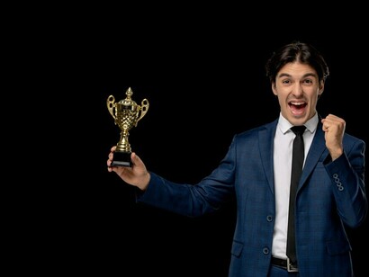 A young, excited businessman in a dark blue suit and tie, proudly holding a trophy, celebrating success