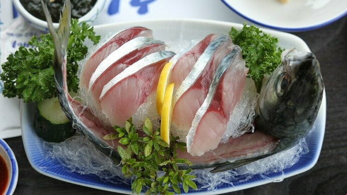 A platter of gleaming raw mackerel sashimi artfully arranged with head and tail intact, showcasing Jeju’s devotion to “hwe” and the island’s celebration of the freshest catch