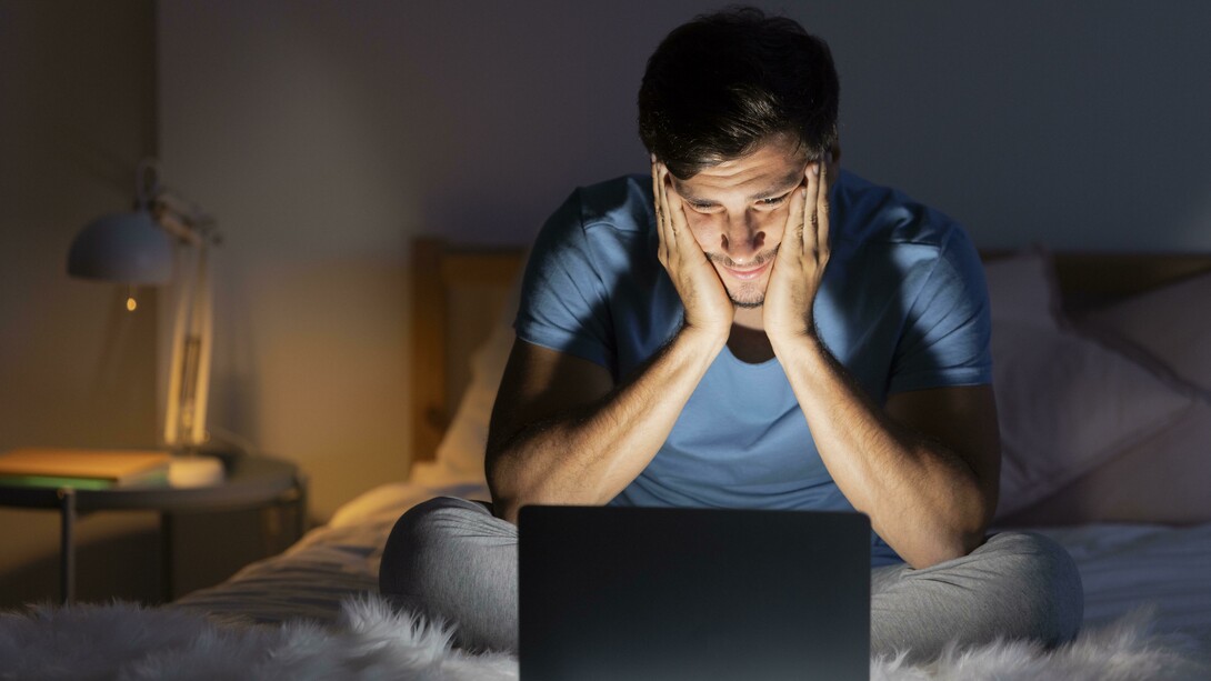 Late at night, a man stares at his computer screen, insomnia keeping him awake