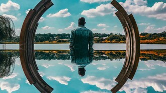 A man's self reflection, framed by a sculpture and the sky