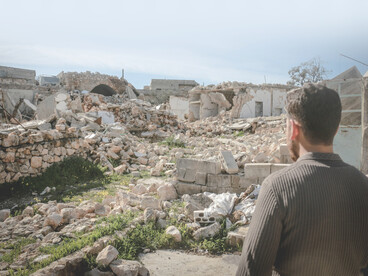 In Idlib, Idlib Governorate, Syria, a man stands among shattered buildings, surveying the ruins left behind by conflict