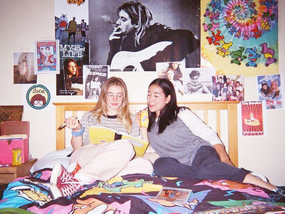 A 90s teenage bedroom covered in posters, with friends relaxing and hanging out