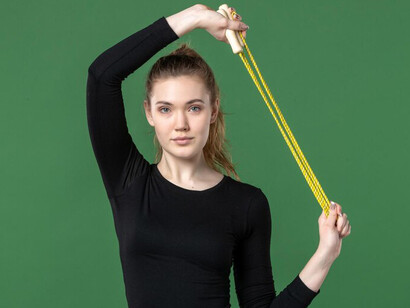 A young female athlete holding a skipping rope on a green background exemplifies the balance student-athletes must maintain between time management for sports and academics while striving to excel in both areas