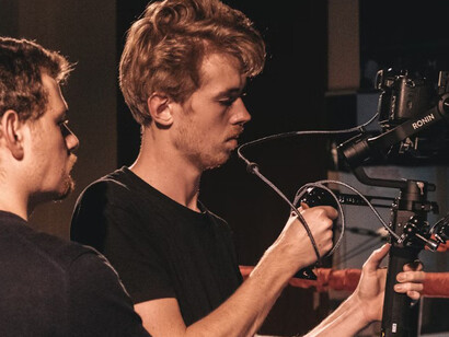 On a Hollywood film set, a man in a black shirt is seen holding a black DSLR camera, working alongside the crew