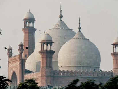 A magnificent morning view of the Badshahi Mosque, its white and red structure framed by trees, captured from the grounds of Minar-e-Pakistan