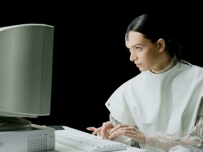 A humanoid robot in a sleek white top interacts with a computer in a high-tech future