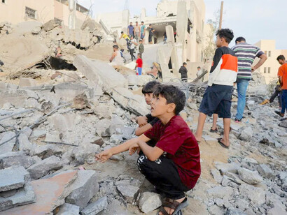 Crianças palestinas sentadas em meio aos escombros enquanto outras revistam um prédio destruído por ataques aéreos israelenses em Khan Younis, no sul da Faixa de Gaza, 2023