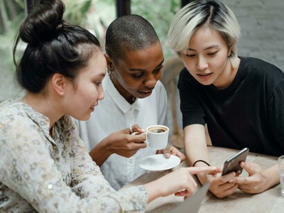 A lively group of diverse women interacting over coffee while using smartphones and tablets—highlighting the everyday influence of social media and online connectivity