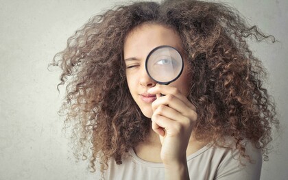 A portrait of a woman holding a magnifying glass over her eye