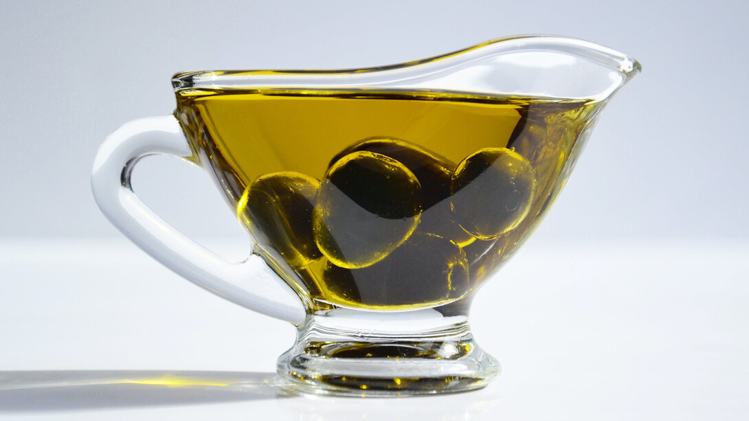 Regador de vidro cheio de azeite de oliva perfumado por azeitonas da estação