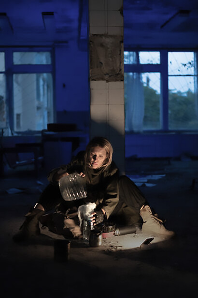 In a haunting portrayal of survival amidst conflict, a lone figure sits within an abandoned building in a war zone, epitomizing the resilience of individuals striving to endure