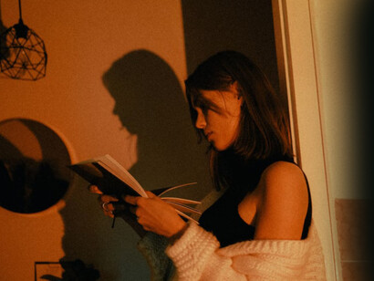 At home, a woman in a white sweater enjoys reading a book
