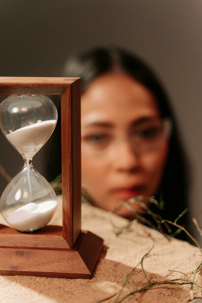 Em um retrato minimalista, a mulher acompanha a passagem do tempo representada pela ampulheta. Envelhecimento e saúde não dependem apenas da idade cronológica, mas também da forma como o organismo responde ao ambiente