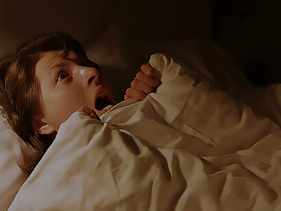 A frightened woman, recently awakened from a nightmare, lies in bed, grappling with fear