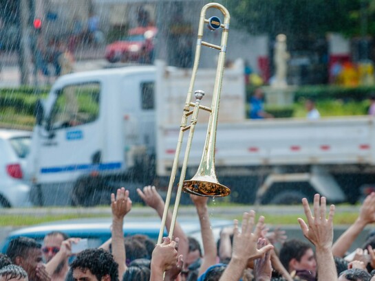 Aglomeração de pessoas com um trombone em destaque entre a multidão. A imagem remete à expressão “botar a boca no trombone”, usada quando alguém torna público aquilo que pensa, denuncia uma situação ou decide falar abertamente sobre algo — um exemplo de como o sentido figurado transforma uma expressão cotidiana