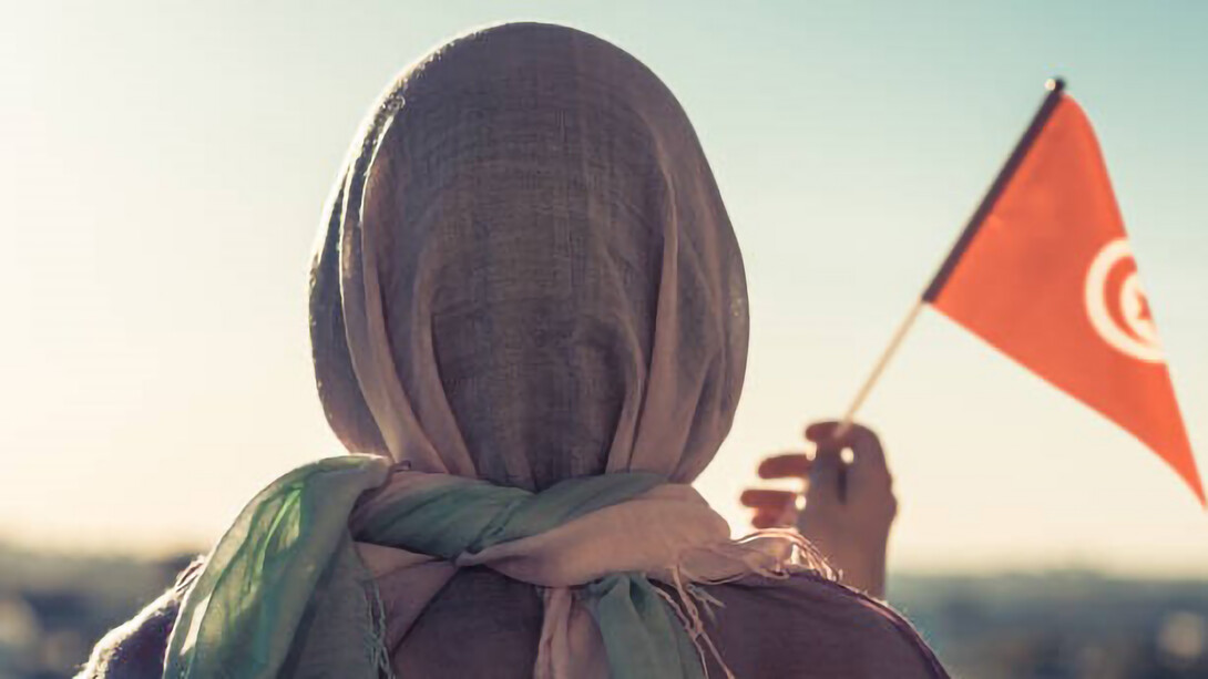 Muslim woman in scarf with Tunisia flag at sunset