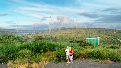 A couple stands in front of a field with wind turbines, that produce clean enery