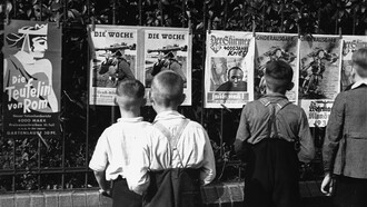 Niños alemanes leen propaganda nazi expuesta en una vía publica
