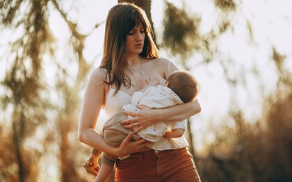 Mulher segura o bebê junto ao corpo em meio à floresta, sob a luz suave do fim de tarde. O vínculo entre mãe e filho está no centro da discussão sobre os benefícios e as características do leite materno