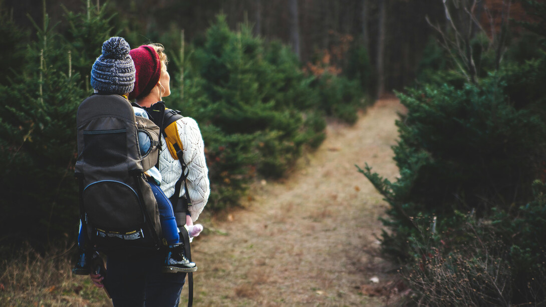 Madre carga su pequeña hija a sus espaldas por un camino campestre