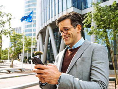 In front of a European Union building, a successful businessman confidently uses his tablet for business activities