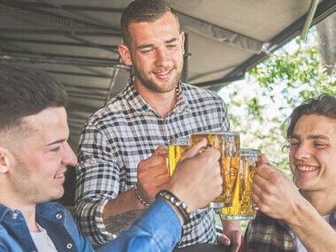 Three male friends enjoying beers together at a pub, sharing a social moment with alcoholic beverages and discussing health