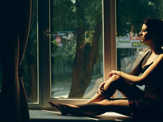 A woman sitting quietly by a sunlit window, representing the emotional patterns carried from childhood into adulthood