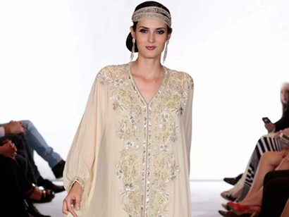 A smiling model wearing a creme caftan from fashion designer Albert Oiknine
