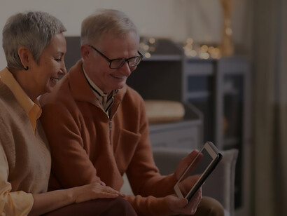 An elderly couple in Europe is looking at a computer screen in their home