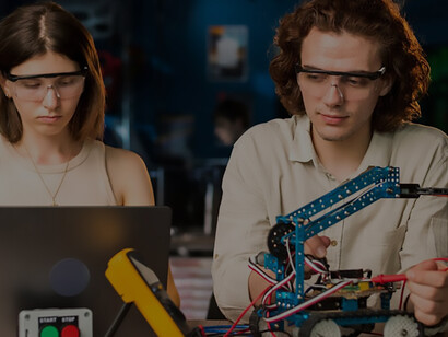 Young man and woman, wearing safety glasses, energetically engage in robotics experiments in a lab, epitomizing immersive STEM learning