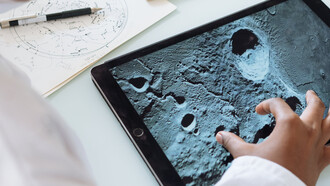 Mão de criança faz movimento de pinça para criar zoom em imagem da lua na aula de ciências