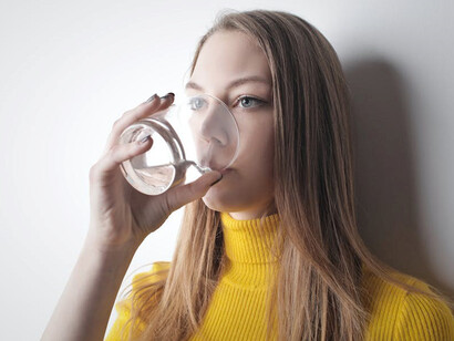 A woman in a sunny yellow t-shirt quenching her thirst with water, maintaining her health and avoiding dehydration